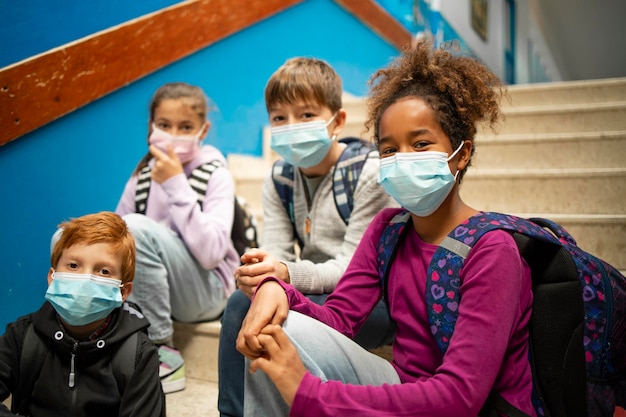 Foto gruppe von schulkindern, die gesichtsmasken tragen und auf den stufen sitzen und auf den beginn des unterrichts warten.