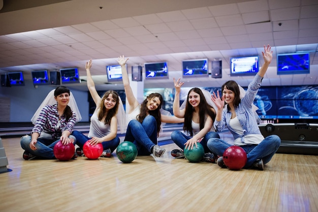 Gruppe von sechs Mädchen mit Bowlingkugeln beim Junggesellinnenabschied im Bowlingclub