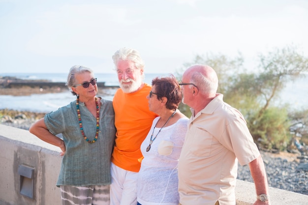 Gruppe von Senioren am Strand, die miteinander reden und Spaß haben - glückliche und reife Leute in Freundschaft oder Beziehung zum Meer oder Ozean im Hintergrund