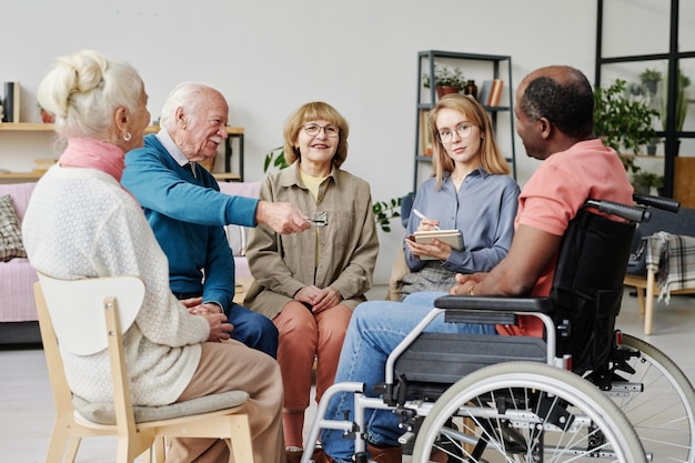 Gruppe von Senioren, die im Kreis sitzen und während der Therapie mit der Pflegekraft im Pflegeheim sprechen