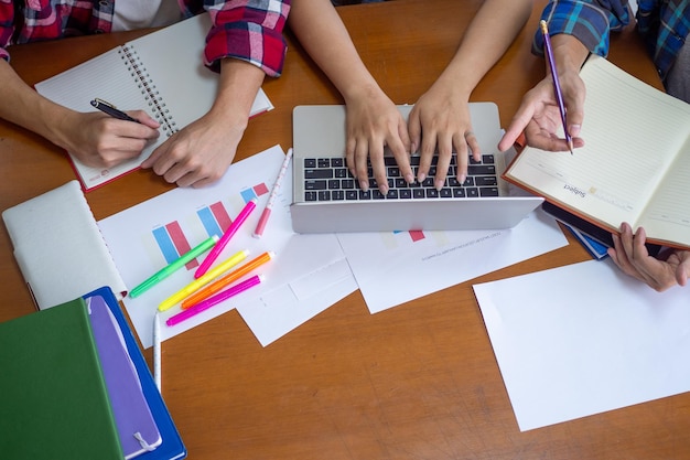 Gruppe von Studenten, die gemeinsam an einem Bericht oder einer Hausaufgabe arbeiten und in der Universitätsbibliothek unterschiedliches Wissen entdecken