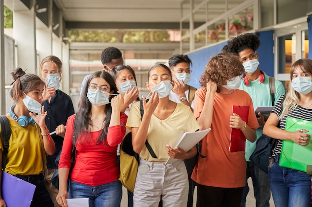 Gruppe von Studenten, die ihre Gesichtsmasken aufsetzen oder abnehmen, junge Menschen verschiedener Ethnien nehmen...