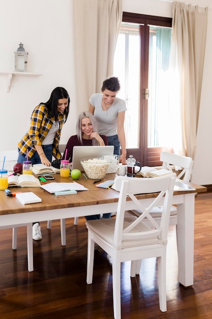 Gruppe von Studentinnen, die sich zu Hause einen Laptop am Tisch teilen