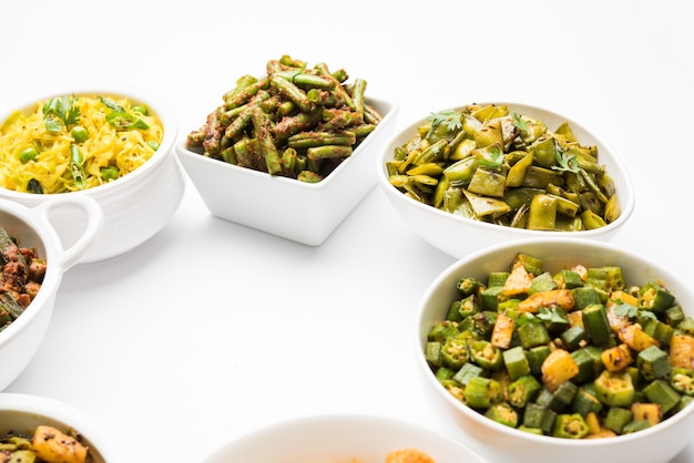 Gruppe von Tawa Fry Sabzi oder Sabji wie Blumenkohl oder Phool Gobhi, Bhindi ODER Okra, Gwar ODER Cluster Beans, French Beans, Kohl oder Patta Gobi, Flat Green Beans, serviert in einer Schüssel. selektiver Fokus