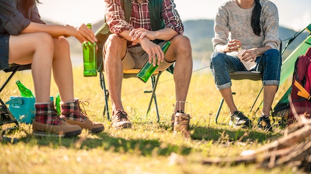 gruppe von touristen, die bierflaschen beim camping klirren. abenteuer, reise, tourismus, freundschaft und personenkonzept.