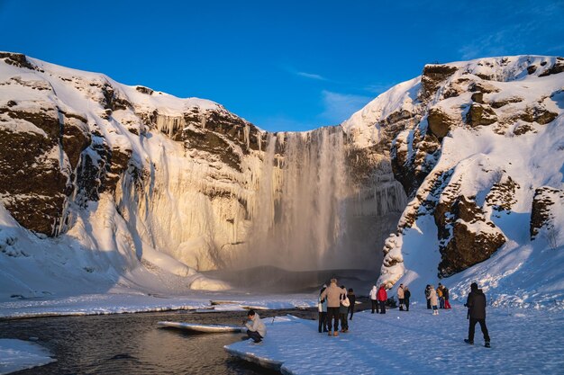 Gruppe von Touristen, die den gigantischen Skogafoss-Wasserfall bewundern, der vollständig mit Schnee bedeckt ist