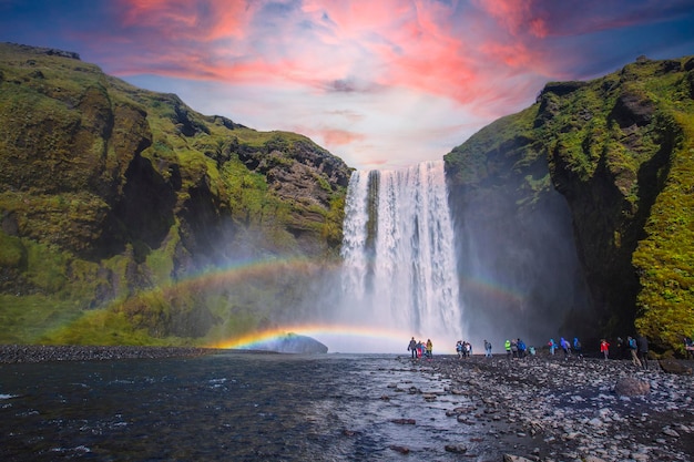 Gruppe von Touristen, die den wunderschönen Regenbogen am beeindruckenden Skogarfoss betrachten