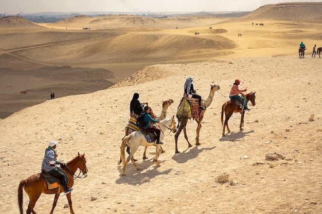 Gruppe von Touristen, die Kamele in der Wüste in der Nähe von Pyramide in Ägypten reiten