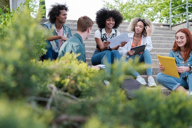 Gruppe von Universitätsstudenten, die auf der Treppe im Freien sitzen und sich unterhalten und lachen Konzept Freundschaft Lebensstil Vielfalt