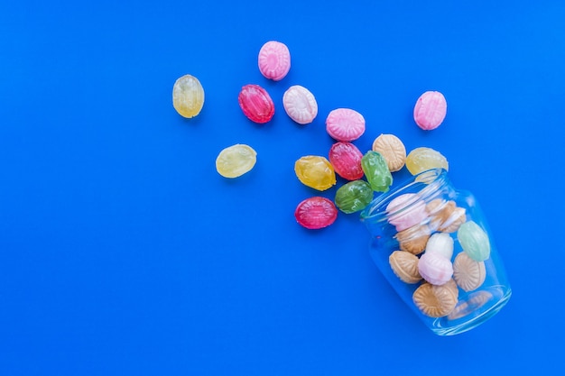 Gruppe von verstreuten bunten Bonbons auf blauem Hintergrund mit Glas. Süßwaren- und Süßwarenladenkonzept. Stock Foto.