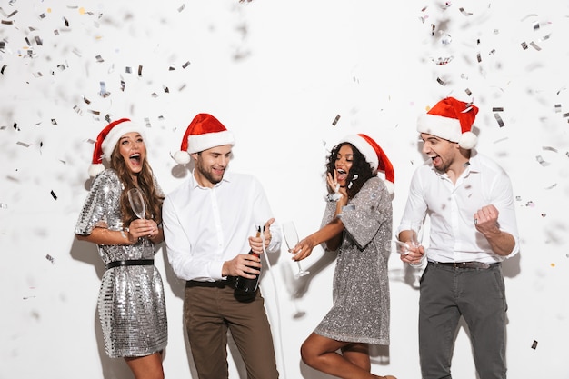 Gruppe von vier fröhlichen, elegant gekleideten Freunden, die isoliert über dem weißen Raum stehen und Neujahr feiern