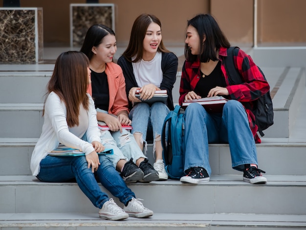 Gruppe von vier jungen attraktiven asiatischen Mädchen-Studenten, die zusammen auf dem Universitätscampus im Freien sprechen und plaudern. Konzept für Bildung, Freundschaft und Studentenleben.