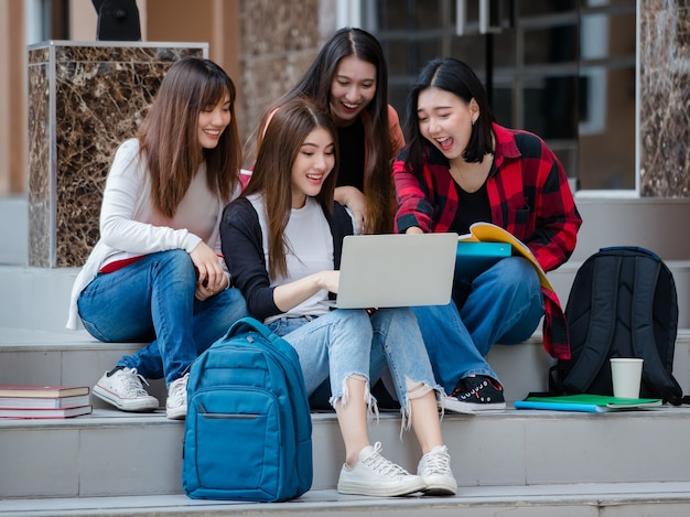 Gruppe von vier jungen attraktiven asiatischen Mädchenstudenten, die zusammen mit Laptop auf dem Universitätscampus im Freien studieren. Konzept für Bildung, Freundschaft und Studentenleben.