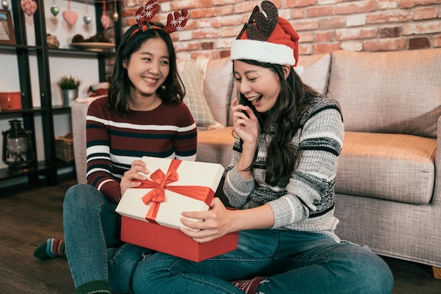 Gruppe von zwei asiatischen Mädchen, die das Konzept der frohen Weihnachten und der frohen Feiertage feiern. schwestern tauschen geschenke aus und senden geschenkboxen zu hause. Freunde sind am Boxtag interessiert, erstaunt und überrascht