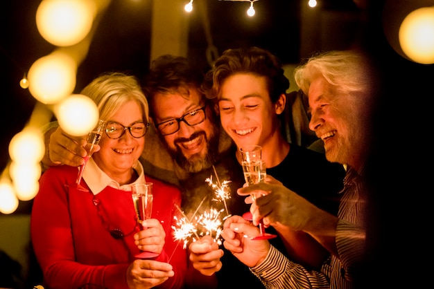 Gruppe von zwei Senioren und zwei Erwachsenen, die zusammen Spaß mit Sparlern haben, um das neue Jahr zu feiern - glückliche Familie mit Lichtern - mit einem Glas Champagner