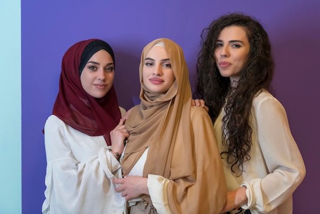 Gruppenporträt schöner muslimischer Frauen, zwei davon in einem modischen Kleid mit Hijab, isoliert auf buntem Hintergrund. Foto in hoher Qualität