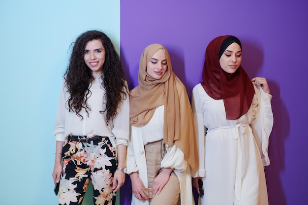 gruppenporträt schöner muslimischer frauen, zwei von ihnen in modischer kleidung mit hijab isoliert auf buntem hintergrund, der moderne islammode und ramadan kareem-konzept darstellt