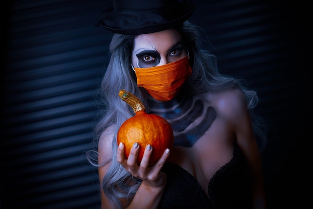 Gruselige Frau in Halloween-Gothic-Make-up mit Gesichtsmaske aufgrund von Covid-19-Beschränkungen mask