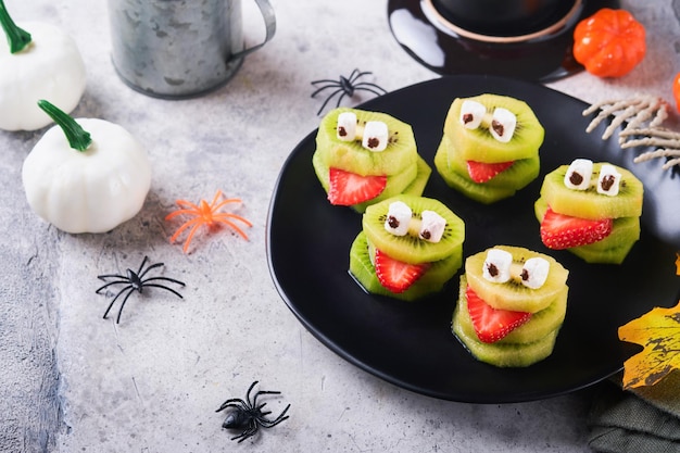 Gruselige grüne Kiwi-Monster für Halloween Gesundes Obst Halloween-Leckereien Halloween-Party Kiwi-Erdbeerapfel und Marshmallow-Monster auf grauem Stein- oder Betontischhintergrund Selektiver Fokus