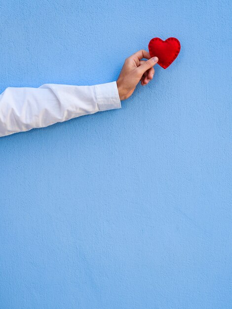 Gruß Valentinstagskarte mit Kopierraum für Text. Das rote Herz in der Hand des Mannes vor dem Hintergrund der blauen Wand