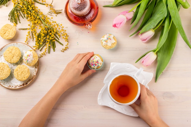 Grußkarte der Frauen Tagesmit Tulpen, Mimose, Tee und kleinen Kuchen auf hölzernem Hintergrund.