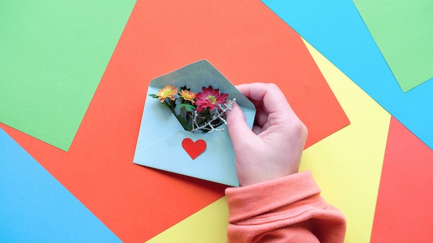 Grußkarte mit Händen, die Umschlag mit Herzform und Blumen halten.