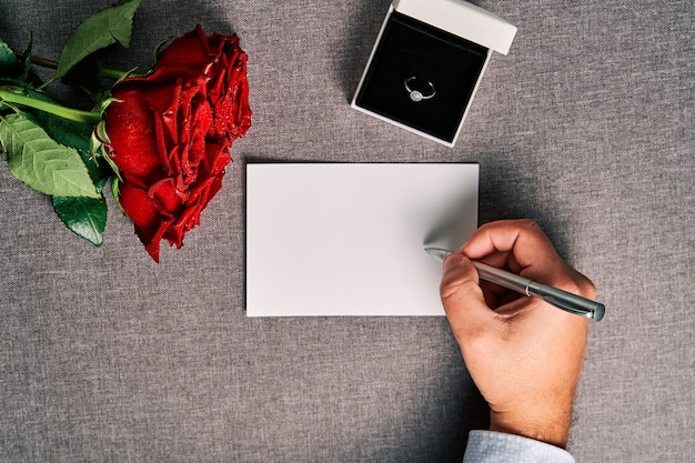 Grußkarte, Verlobungsring und rote Rosen als Geschenk. Konzept des Valentinstags und der Ehe.