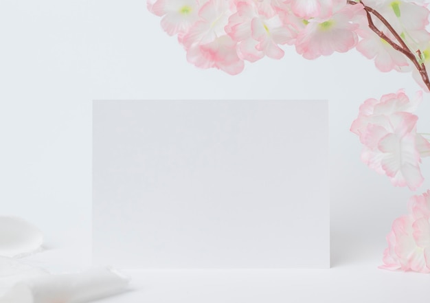 Grußkarten-Mock-up-Dekoration mit weißer Blume Vorderansicht Blanko-Papierkarte auf einer Holzplatte und weißem Hintergrund