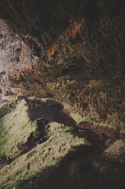 Gruta de cascada en Islandia con colores marrones y grises en un camino con gente en el fondo