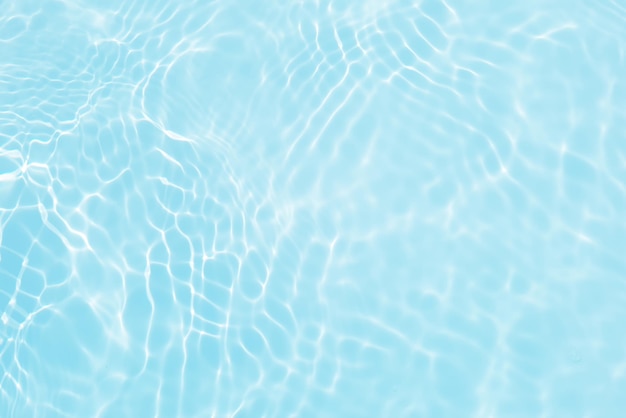 Água azul em uma piscina com ondulações e o sol refletindo na superfície.