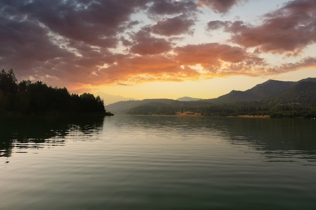 Água calma do lago e um lindo nascer do sol sobre as montanhas e a floresta