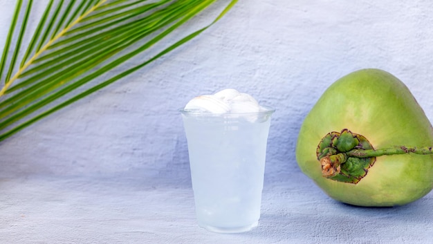 Água de coco gelada em um copo de plástico e coco no fundo branco