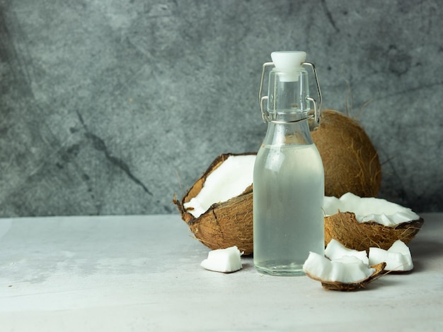 Água de coco refrescante fresca em uma garrafa com um coco aberto com polpa branca em um fundo de concreto