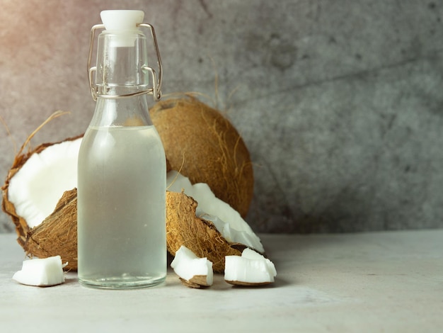 Água de coco refrescante fresca em uma garrafa com um coco aberto com polpa branca em um fundo de concreto