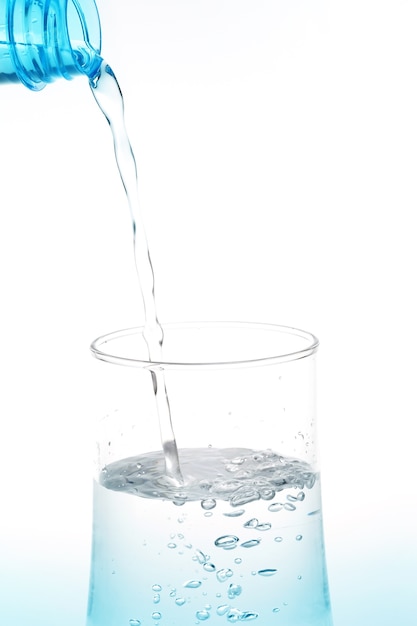 Água de derramamento da garrafa no vidro no fundo branco.