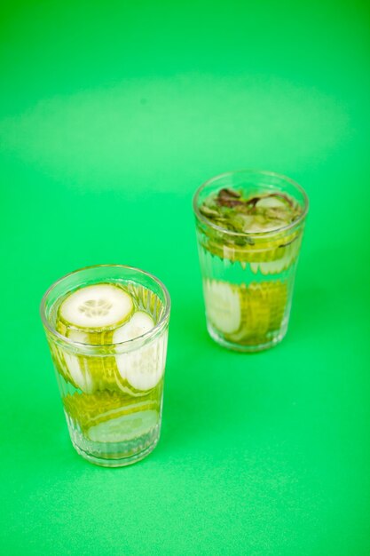 Água desintoxicante caseira fresca nutritiva de pepinos orgânicos em dois copos contra um fundo verde