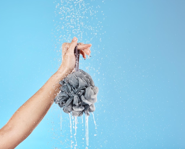 Água do chuveiro e mãos com uma bucha para limpeza de bem-estar de luxo e aliciamento contra fundo de estúdio azul Cosmético de saúde e mulher com produto para cuidados com o corpo e tratamento com espaço de maquete