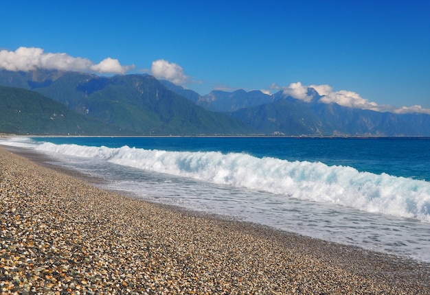 Água do mar azul clara com onda branca da espuma na praia do cascalho na costa em Taiwan.