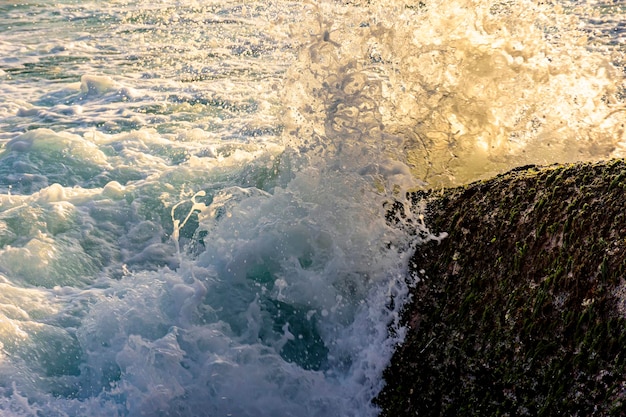 Água e espuma marinha salpicando com as ondas batem contra as rochas durante o pôr-do-sol tropical