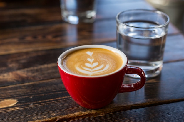 Água e xícara de café vermelha com latte art na mesa de madeira. Mesa no café. Conceito de café da manhã fácil. Copo e copo pequeno de cerâmica