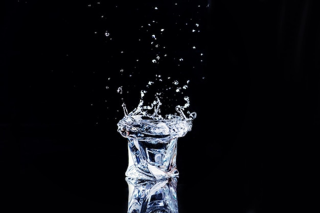 Água em um copo com esguicho e cubos de gelo em fundo preto