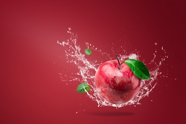 Água espirrando na maçã vermelha fresca no vermelho