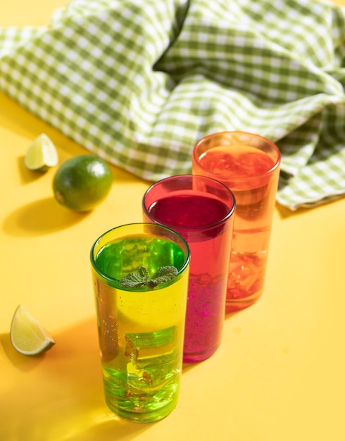 Água fresca de limonada de coquetel de verão com frutas cítricas de menta e limão em copos coloridos em fundo amarelo