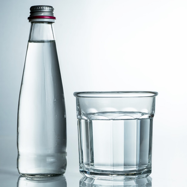 Água fresca e fria, pura em um copo com uma garrafa. Água purificada em um copo sobre uma mesa cinza. água na mesa cinza.