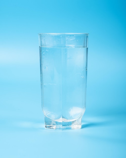 Água limpa em um copo de vidro fechado em um fundo azul