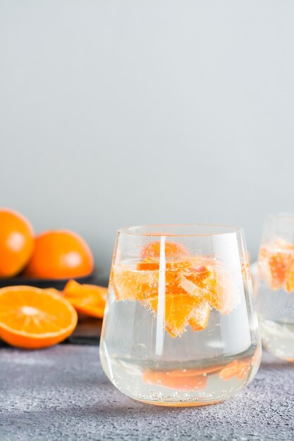 Água mineral de coquetel sem álcool com pedaços de tangerinas em um copo e frutas maduras ao lado da mesa. Comida de desintoxicação. Copie o espaço. Visualização vertical