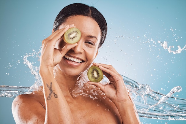 Água para a pele e retrato de mulher com kiwi para produtos de beleza orgânicos e saudáveis naturais em estúdio Dermatologia bem-estar e menina com respingos de água de frutas e cosméticos em fundo azul