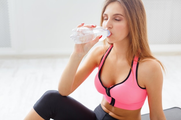 Água potável de mulher jovem esporte. Garota fitness confiante segurando uma garrafa de plástico, com sede após o treino, conceito de estilo de vida saudável