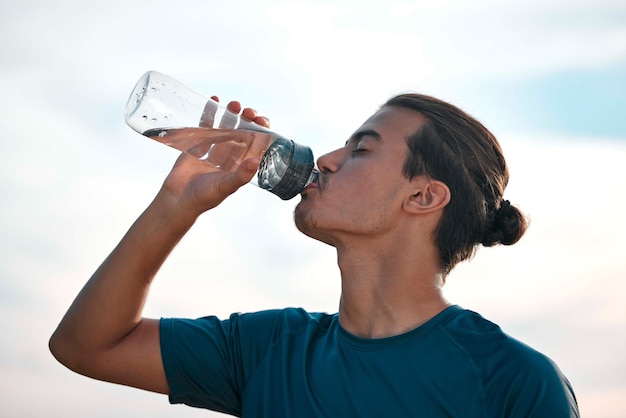 Água potável e homem com exercício de treinamento e treino para equilibrar estilo de vida saudável e sede Atleta masculino e corredor com água líquida e hidratação após o pôr do sol e o céu