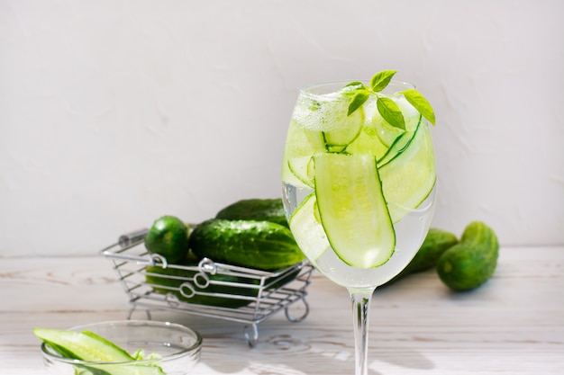 Água refrescante com fatias de pepino e manjericão folhas em um copo e pepinos em uma cesta na mesa